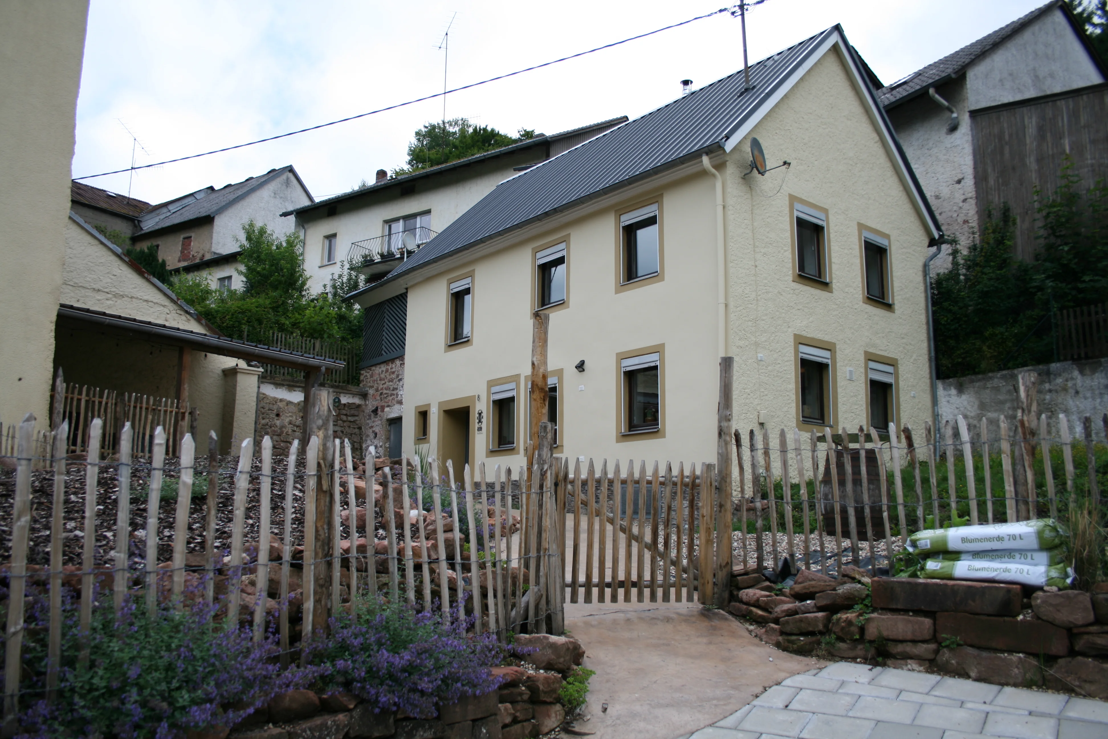 Vakantie huis in de eifel buitenzicht, houten hekjes, grote voortuin met terras, houtsnippers lang looppad en groen.