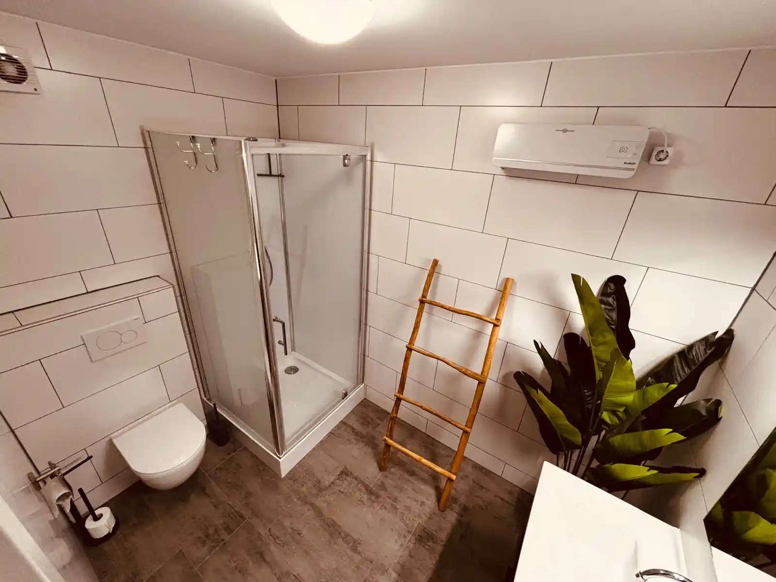 Een badkamer in het vakantiehuis in de eifel met een douche, een toilet, een wastafel met belichte spiegel, een heater en plant.