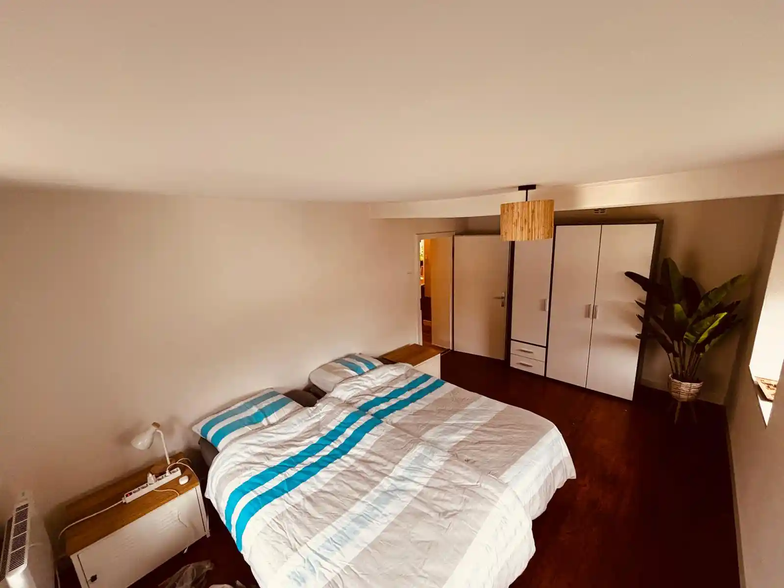 Een slaapkamer in de eifel met een 2 persoonsbed, een grote kledingskast, nachtkastjes, lamp en plant met mooi uitzicht over het dorp in de eifel duitsland.