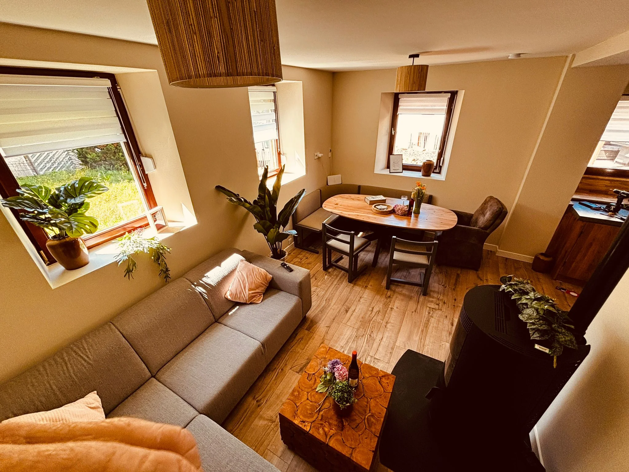 Een angle shot van de woonkamer met een grote zitbank, een tafel met 3 stoelen, een eettafel hoekbank. Verder is er in de foto de kagel te zien en een klein bijzet tafel bij de bank. Dit alles in een thematisch huis gelegen in de eifel voor gezinnen en dierenvrienden.